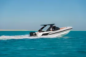 Side view of a white and black speedboat racing across the sea, kicking up a trail of white foam.