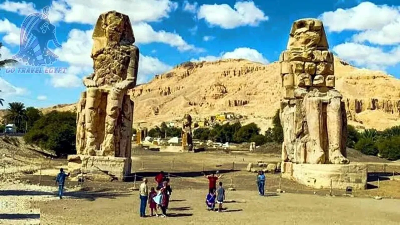 Colossal ancient Egyptian statues flank a row of massive stone columns at Luxor Temple, with a single tourist walking through the quiet courtyard in early morning light.