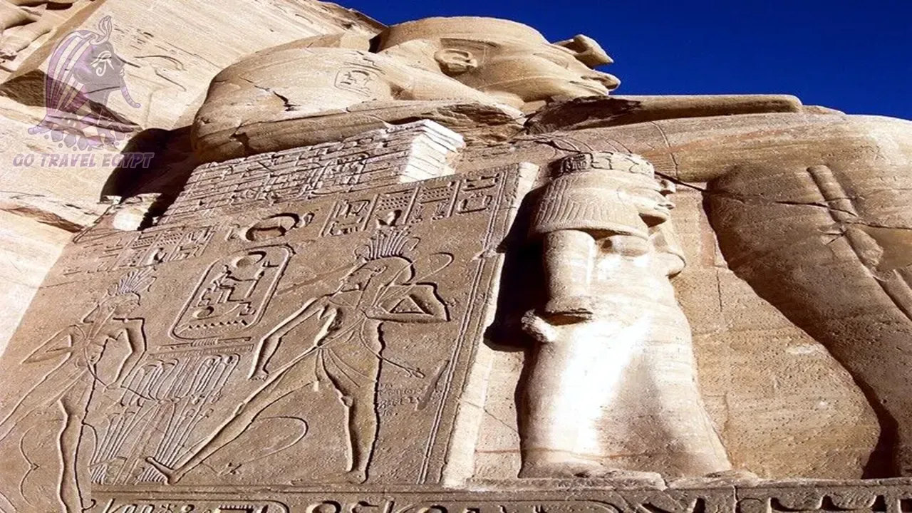 Two tall seated pharaoh statues wearing double crowns stand at the entrance corridor of Luxor Temple, with rows of columns receding into the distance and tourists gathered below.