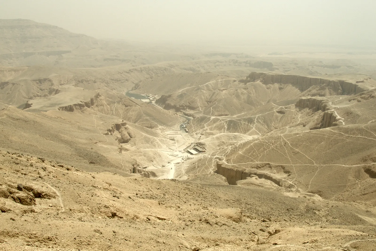 A long paved causeway leads up to the three-tiered Temple of Hatshepsut, built into sheer cliffs at Deir el-Bahari, with a small sphinx statue beside the ramp.