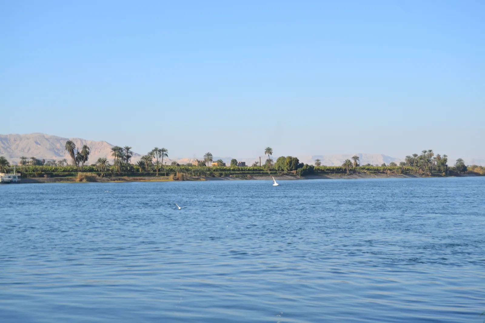 A couple sits at the bow of a felucca watching a pink and orange sunset over the Nile in Luxor.