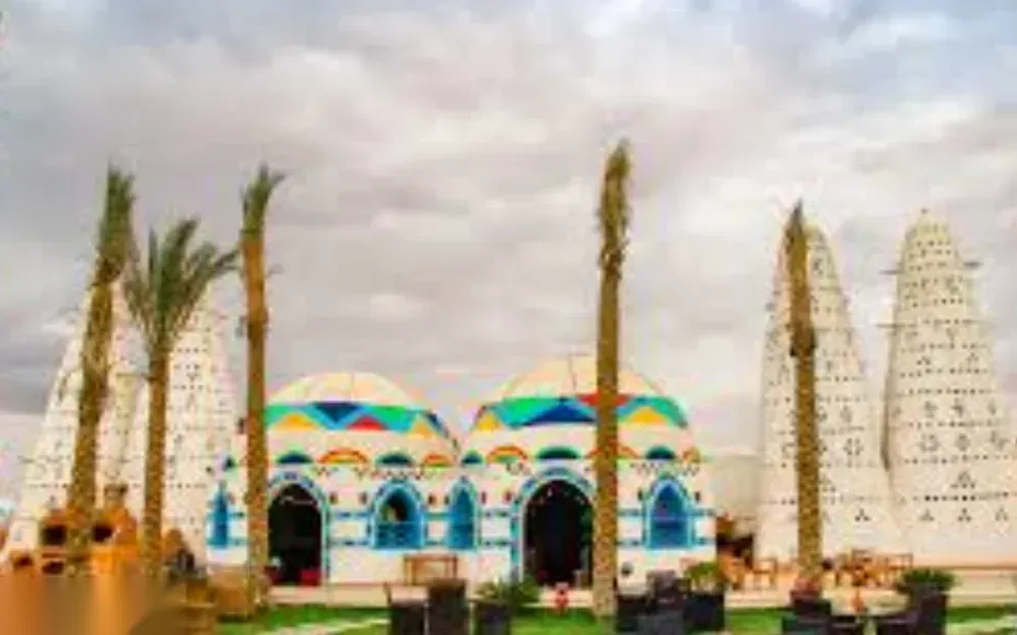 A blurred view of the same colorfully domed Nubian buildings and cone-shaped towers seen from a slightly different angle, with palm trees in front.