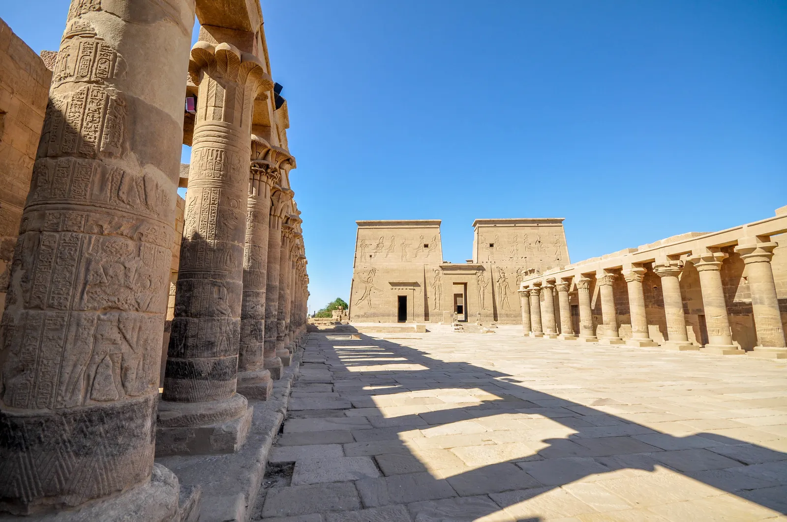 Trajan's Kiosk at Philae Temple stands with its tall columns and floral capitals under a bright blue sky with wispy clouds.