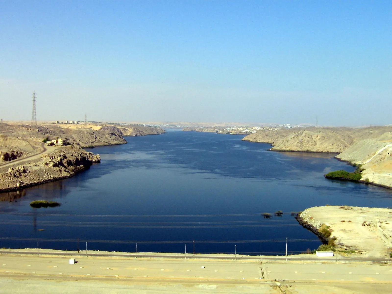 Aerial view of Philae Temple's island complex surrounded by the waters of Lake Nasser, with small tour boats docked at its shore.