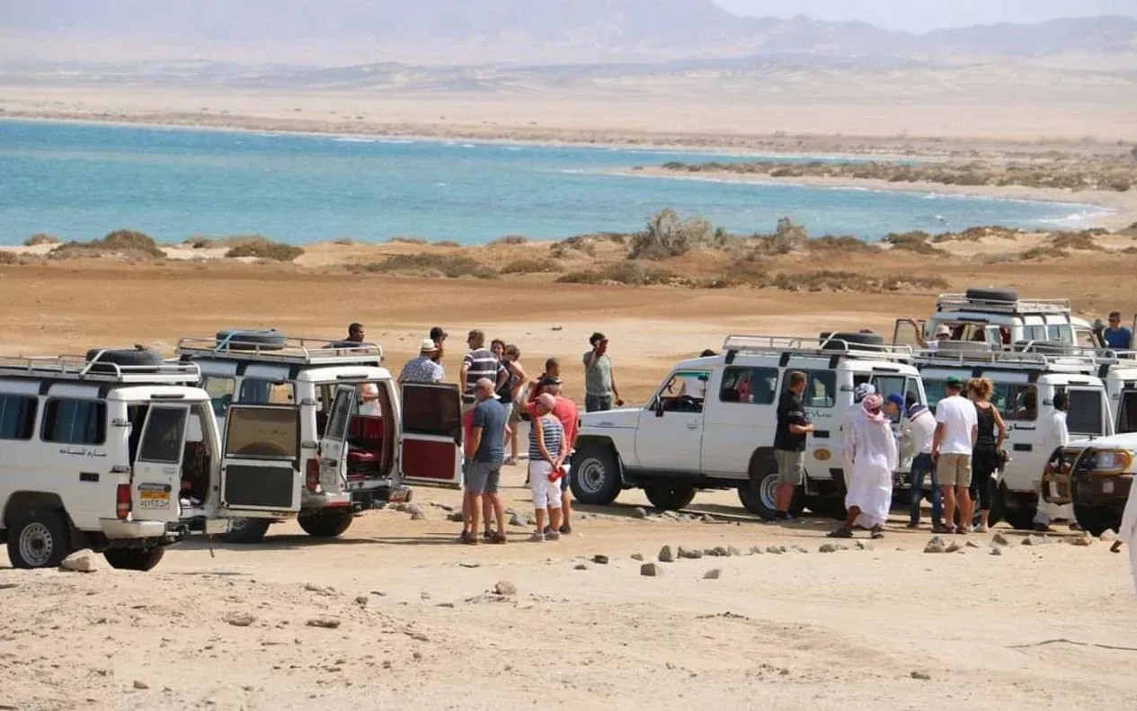 Acacia trees scattered across a desert plain with mountains in the background and tourists seated in the foreground.