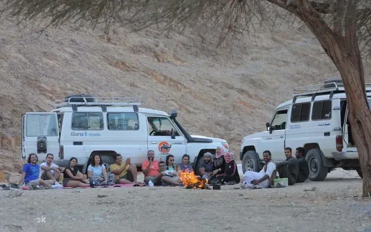 A white 4x4 vehicle driving fast across an open desert plain, kicking up dust, with mountains behind.