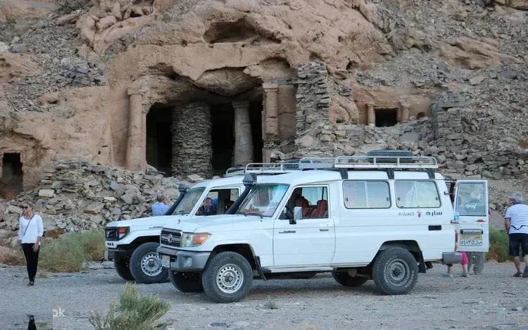 Convoy of 4x4 vehicles parked beside a turquoise lagoon with tourists and a Bedouin guide gathered nearby.