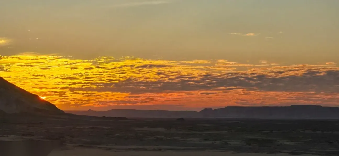 Wide sunset sky with streaks of orange and gold clouds over the dark desert horizon.