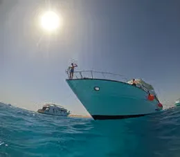 White yacht named Mermaid cruising with crew members on deck and a coastal town visible in the background.