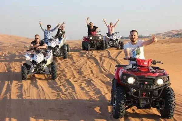 Two red quad bikes parked side by side on sand under a clear blue sky.