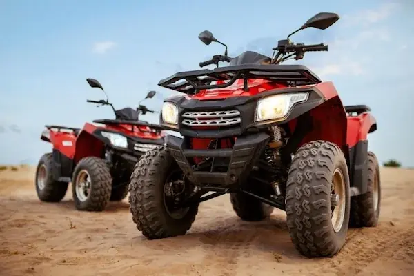 Group of six riders on quad bikes cheering with arms raised on a sandy desert trail.