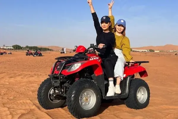 Two women sharing one red quad bike, both throwing up peace signs with other quad bikes visible behind them.