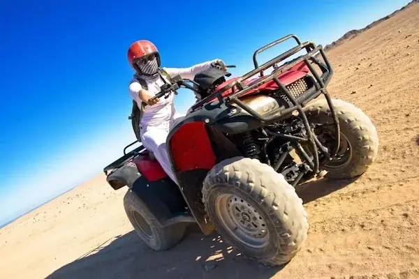 Rider in a white outfit and red helmet turning a quad bike on a sand dune.