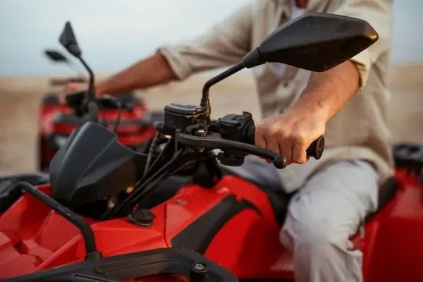 Close-up of a rider's hands gripping the handlebars of a red quad bike.
