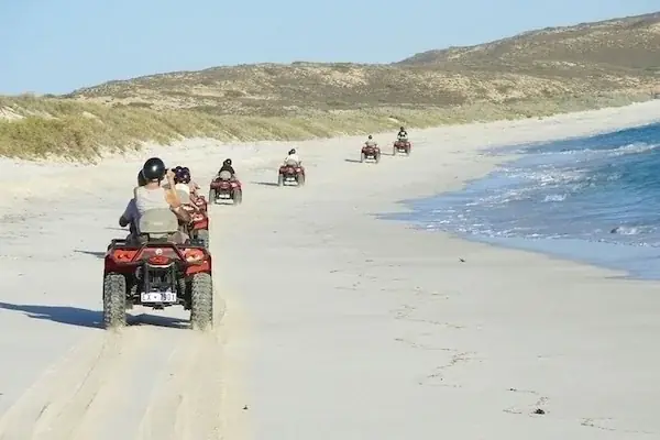 A row of parked quad bikes with riders adjusting their headscarves in a desert valley between rocky mountains.