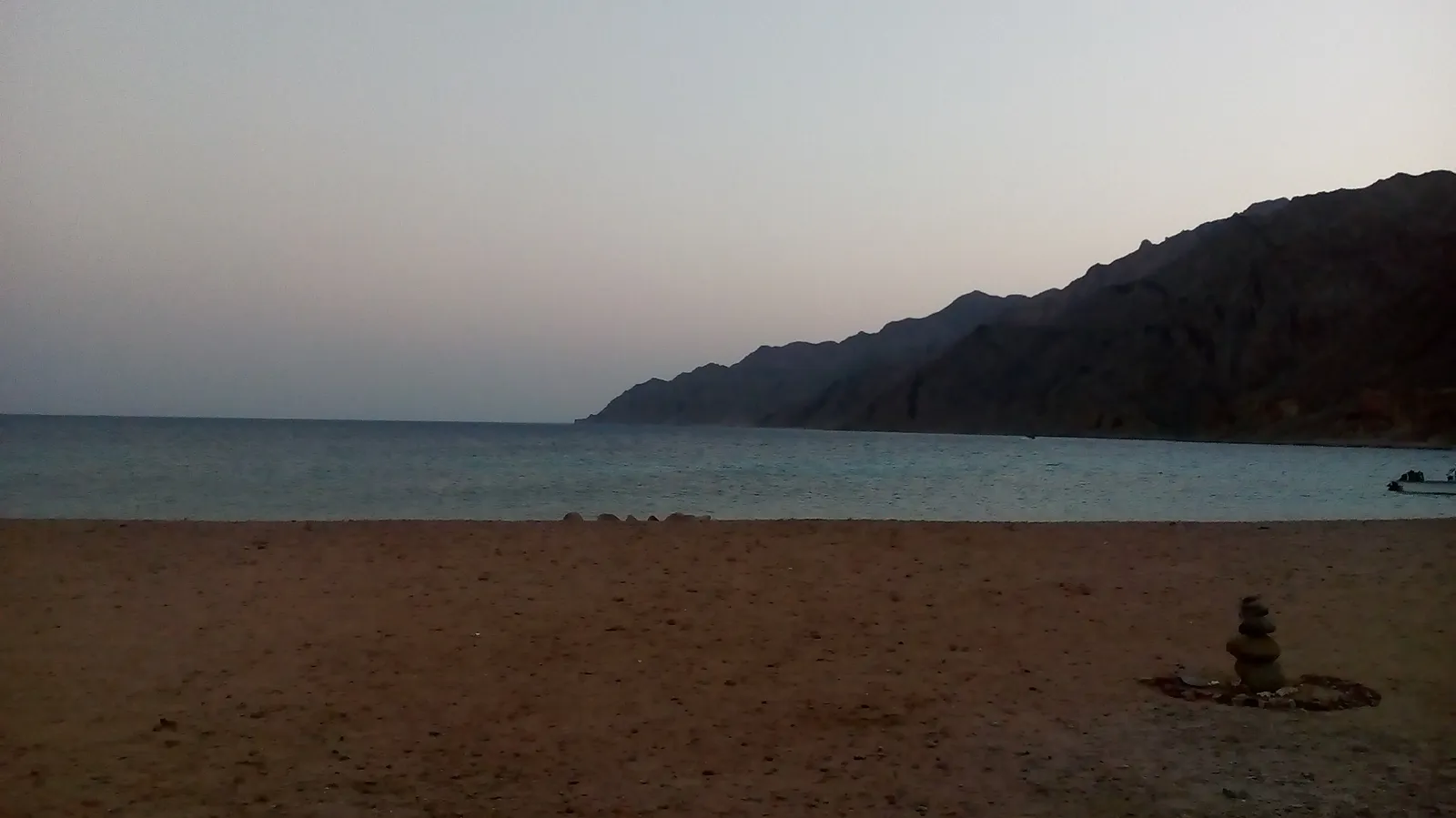 View from a hillside over a curved bay with dive boats moored offshore and rows of straw beach umbrellas on the sand.