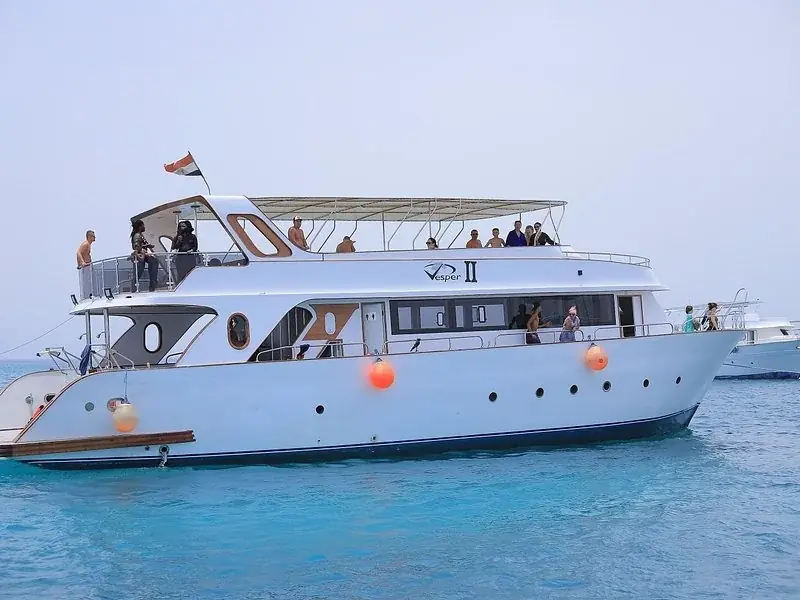 The boat Vesper II underway with passengers standing on the upper deck, an Egyptian flag flying from the mast.