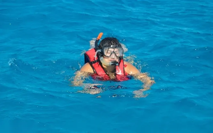 A snorkeler wearing an orange life vest and mask floats at the surface of deep blue water.