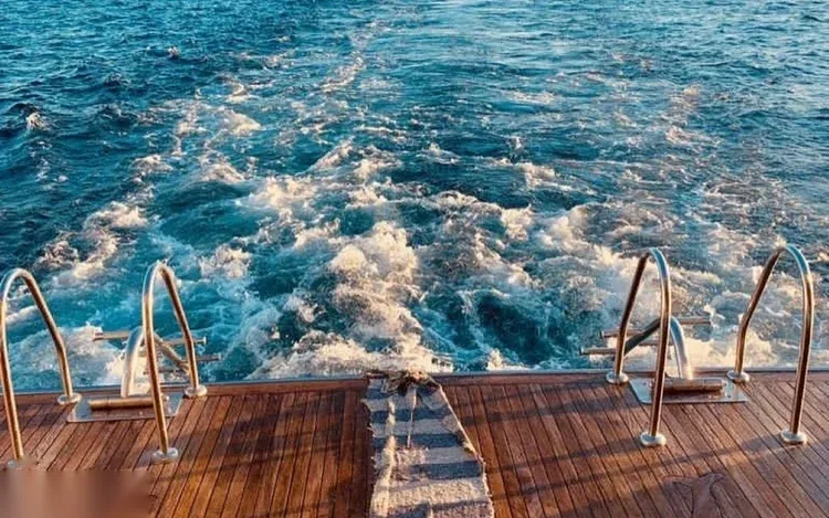 View of a boat's stern with dive ladders and frothy white wake water behind it.