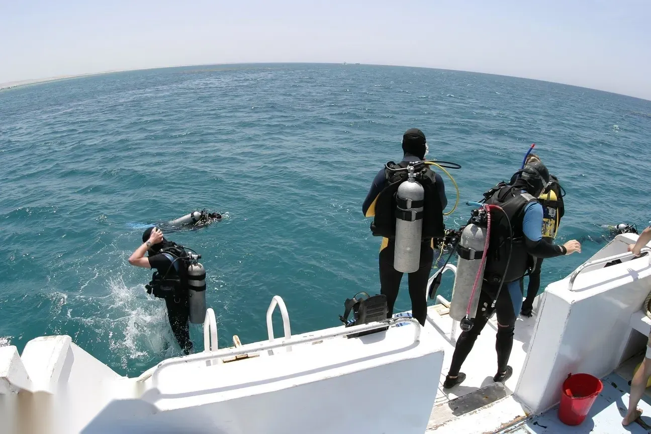 Divers enter the water from a dive boat platform, one already submerged and others waiting with tanks on.