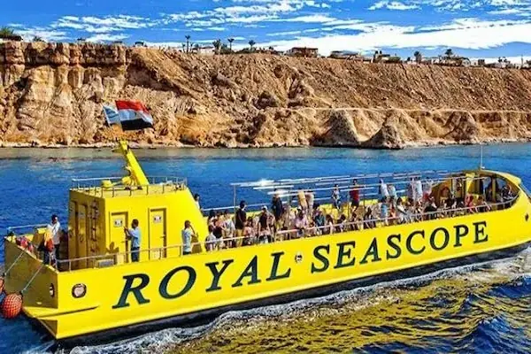 Royal Seascope boat with Egyptian flag cruising past a dramatic reddish rocky coastline under a partly cloudy sky