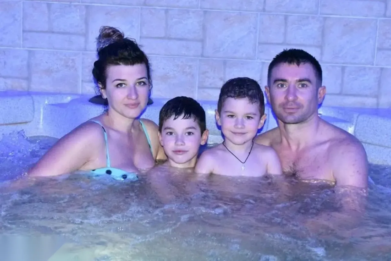Family of four smiling together while soaking in a bubbling jacuzzi with tiled stone walls lit in purple light
