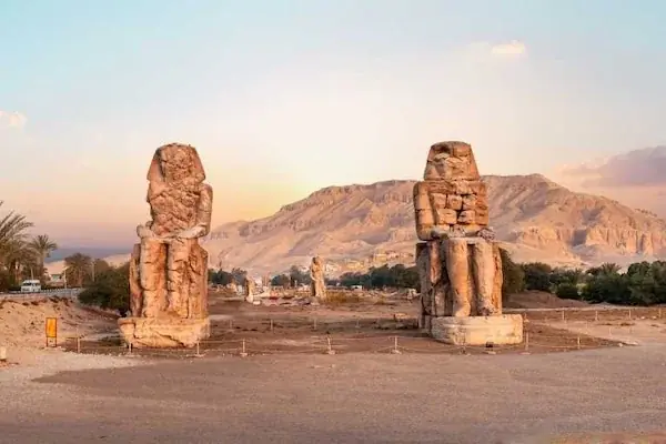 Pylon entrance of Luxor Temple flanked by seated pharaoh statues and a tall obelisk against a clear blue sky