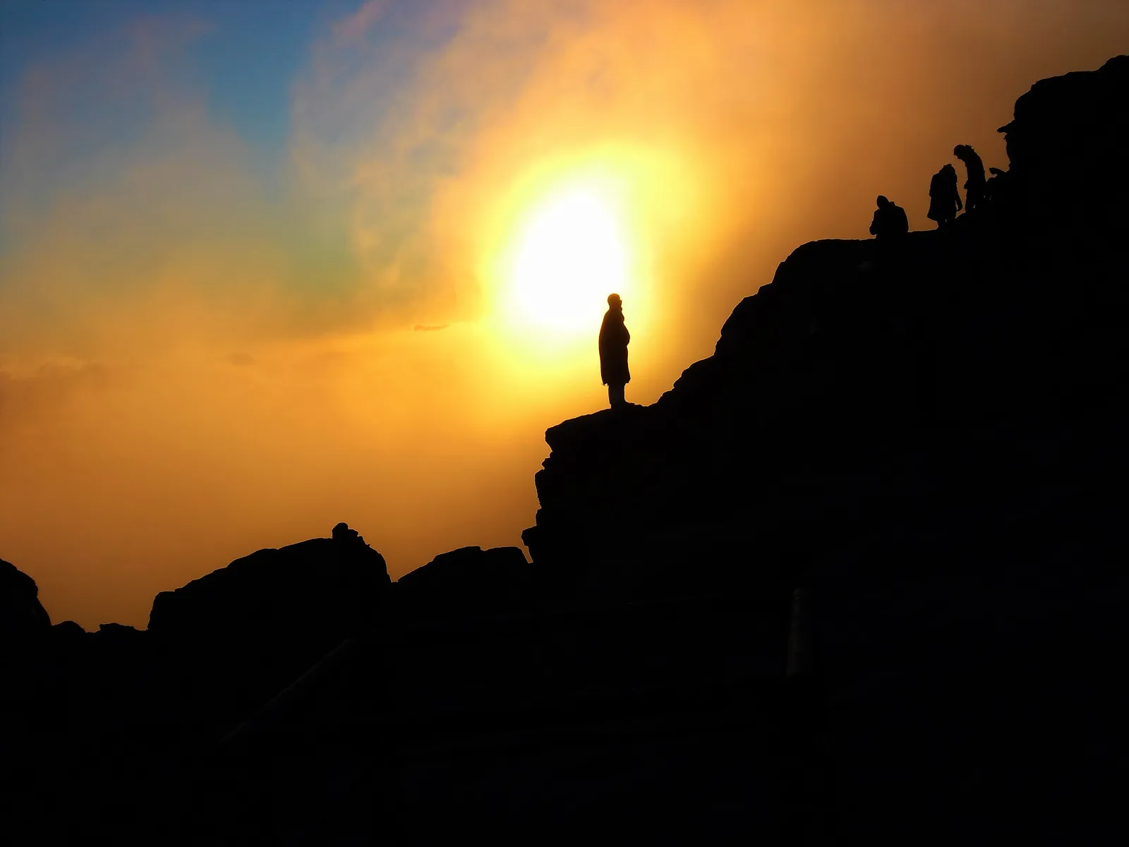 Group of bundled-up hikers standing on rocky outcrops watching the sun rise over layered desert mountains