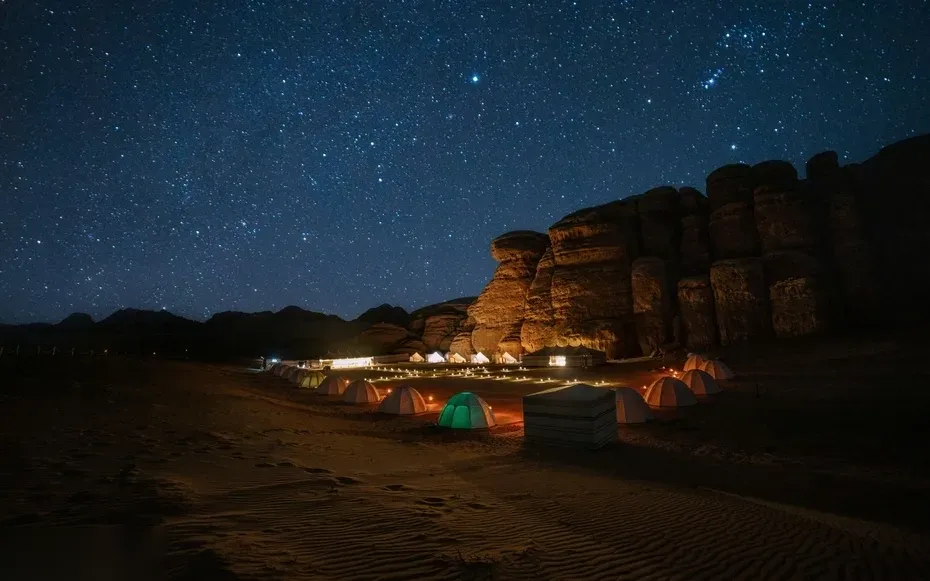Group of guests seated on cushions around a low table with candles and snacks under a dark starry desert sky