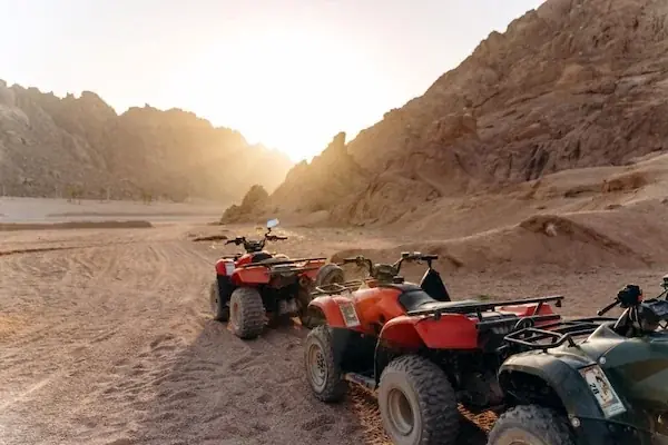 Six tourists sitting on red quad bikes posing together as the sun sets over the desert