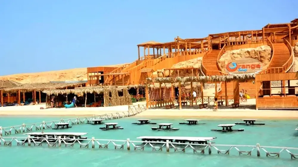 Wide view of the Orange Bay wooden resort complex built into a sandy hillside above a turquoise beach