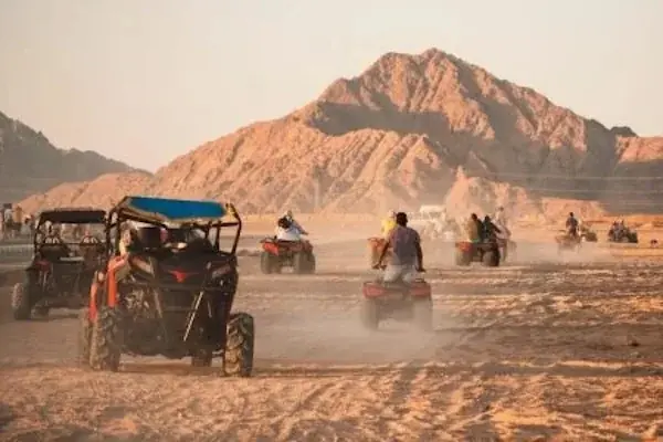 Convoy of dune buggies and quad bikes kicking up dust across the desert with mountains in the background