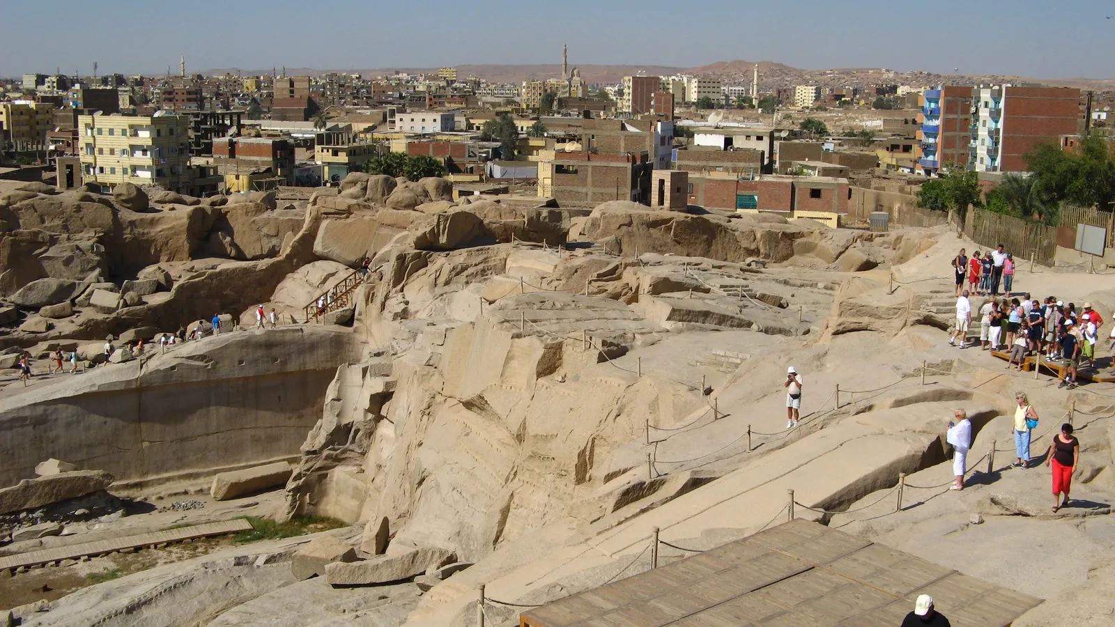 Close-up view down into the granite quarry trench surrounding the Unfinished Obelisk with a roped walkway and city buildings in the background