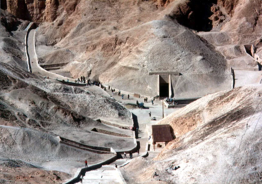 Wide view of sandstone cliffs and excavated tomb entrances surrounded by low mudbrick retaining walls in the Valley of the Kings