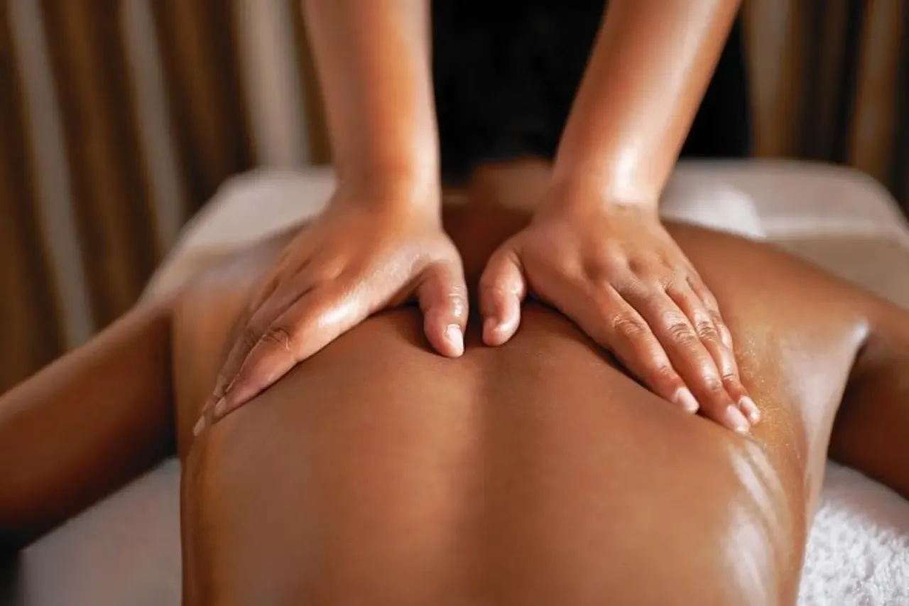 Three women lying face down on marble tables having chocolate body wraps applied by spa therapists in a lantern-lit hammam room
