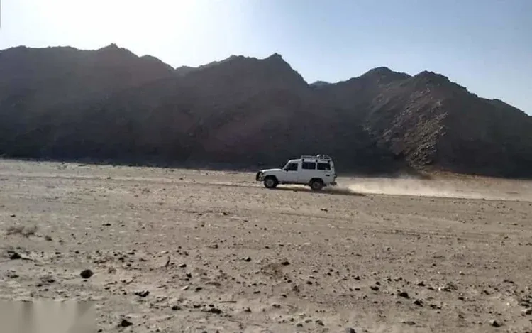 White 4x4 jeep speeding across an open desert plain kicking up a trail of dust with mountains in the distance