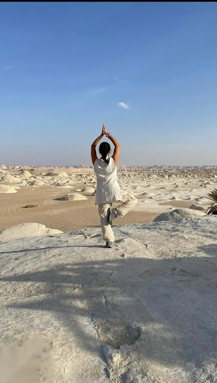 Woman practicing a yoga tree pose on a white rock formation overlooking the vast White Desert landscape