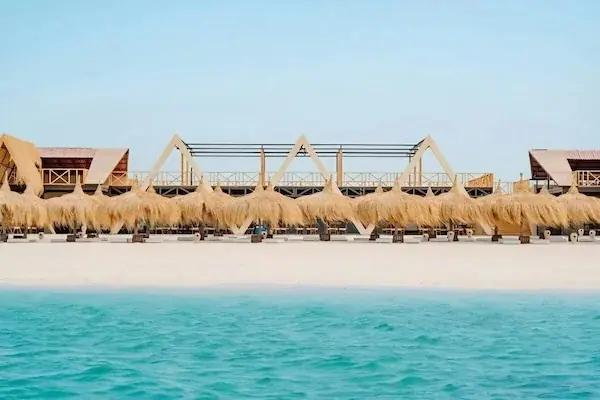 Group of eight tourists and two dive guides standing in shallow turquoise water wearing snorkel masks and fins, a boat visible behind them