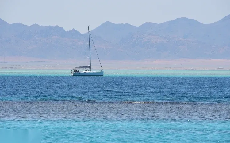 Aerial view of a white yacht anchored near dark coral patches close to a bright white sandbar island